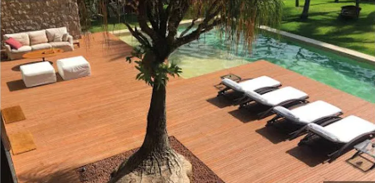 Amplo deck ao redor de piscina com árvore central e espreguiçadeiras